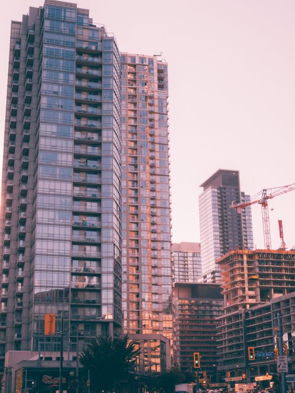 PISOS Modern skyscrapers in an urban downtown with construction cranes at sunset.